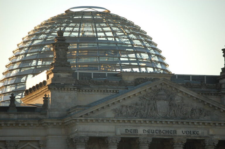 Glaskuppel und Steinfassade des Reichstagsgebäudes in Berlin. Auf der Fassade ist der Schriftzug "Dem deutschen Volke" eingraviert.